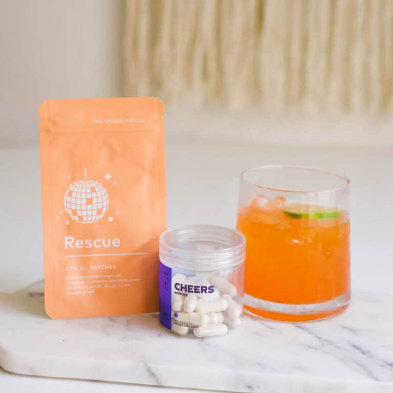 A cocktail next to a bottle of Cheers Restore and a Rescue Patch from The Good Patch.