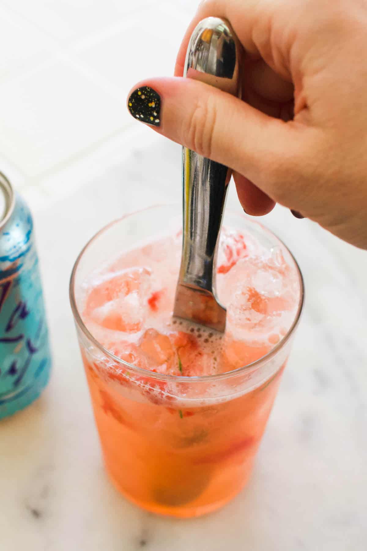 Woman giving a strawberry mocktail a stir with a knife.