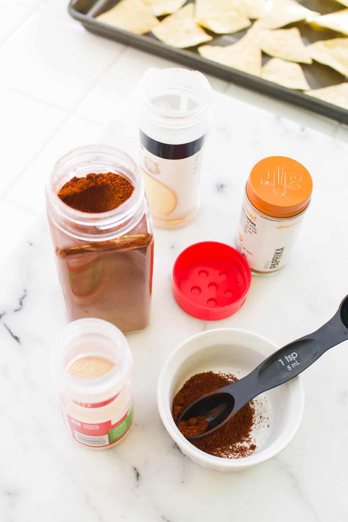 Open jars of spices next to a small bowl of DIY spice seasoning for tortilla chips.