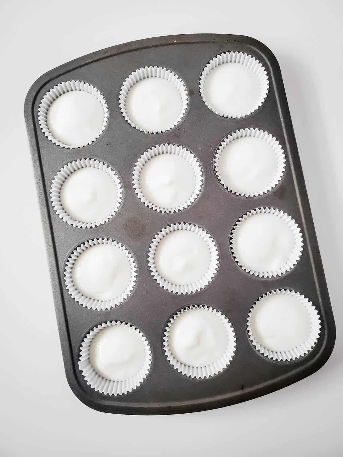 A cupcake pan with white liners filled with angel food cake mix batter.