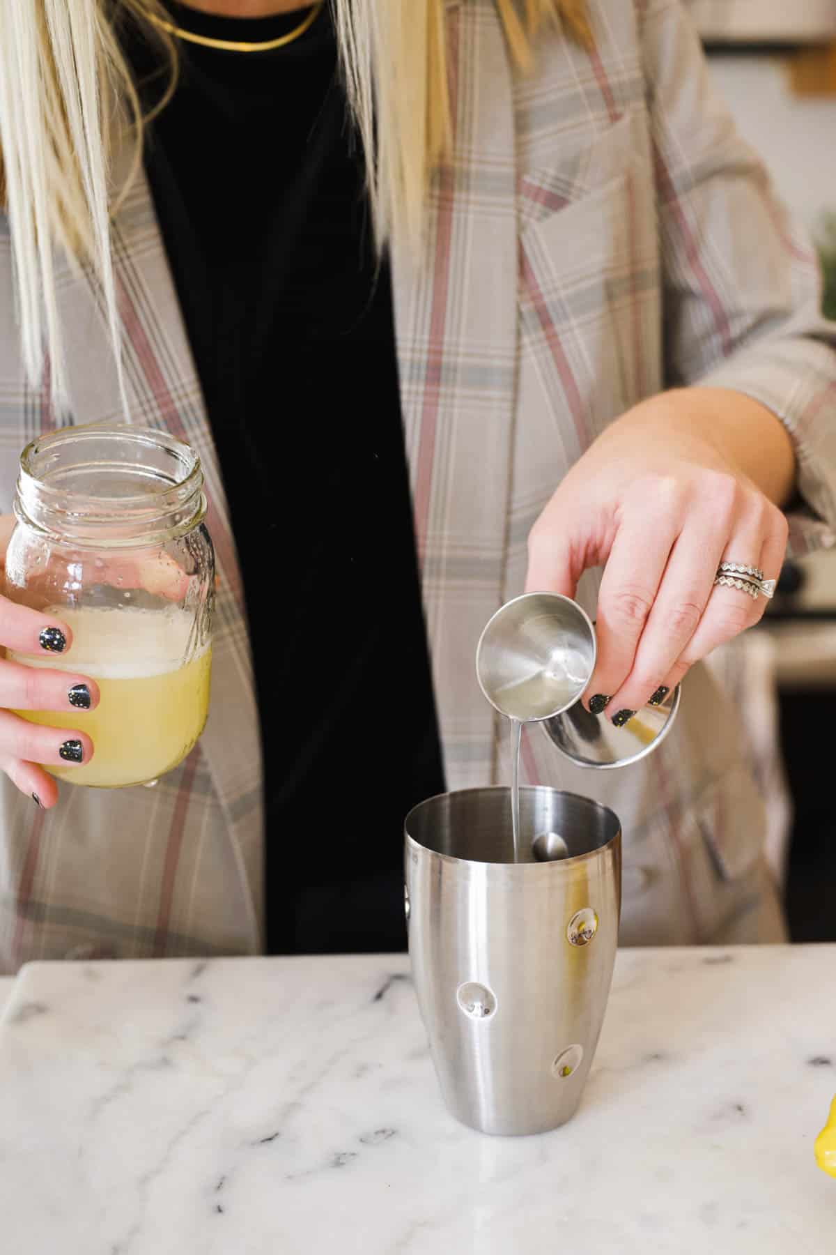 Woman measuring fresh lemon juice into a cocktail shaker.