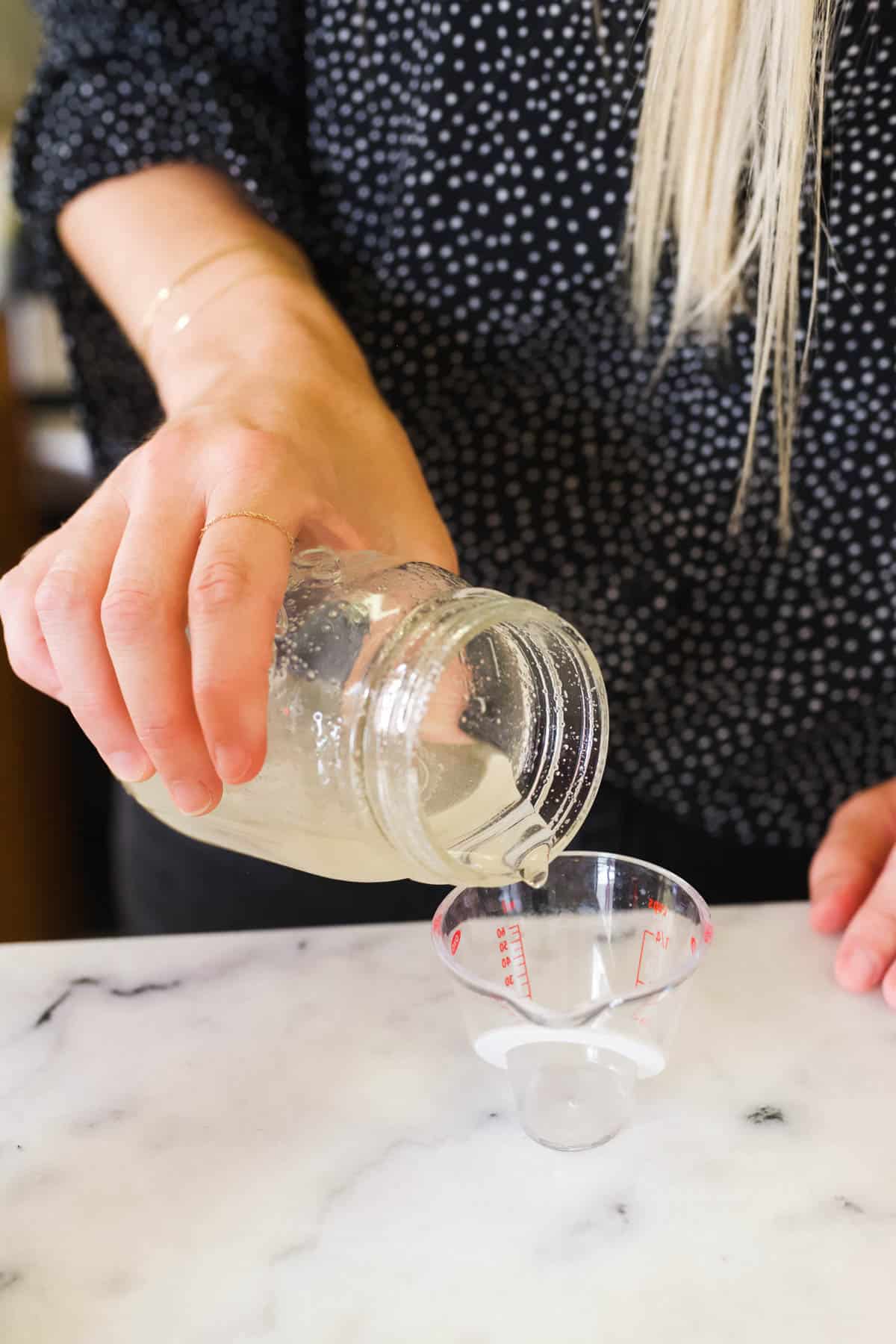 Woman pouring a jar of simple syrup into a measuring cup.