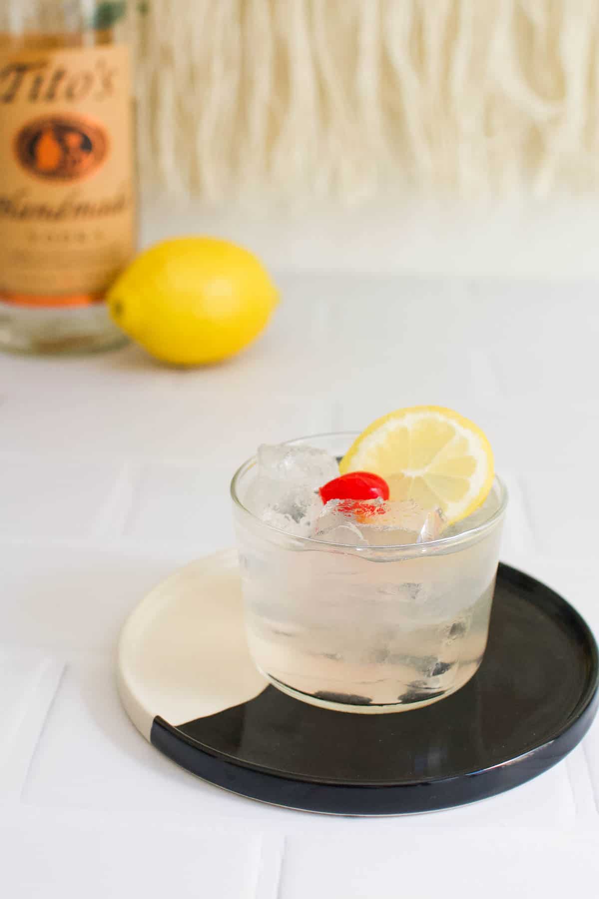 Vodka Sour on a black and white tray with a lemon and bottle of vodka in the background.