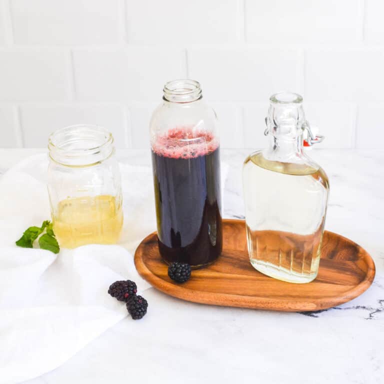 homemade simple syrups on a table with a wooden tray and some fruit and herbs.