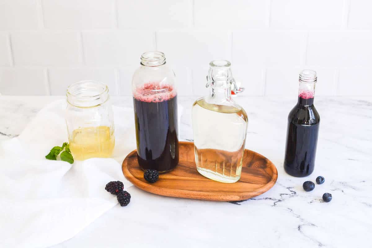 4 types of flavored simple syrups for cocktails on a table with fruit around it.
