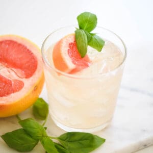 Close up of a grapefruit cocktail garnished with fresh grapefruit juice and basil.