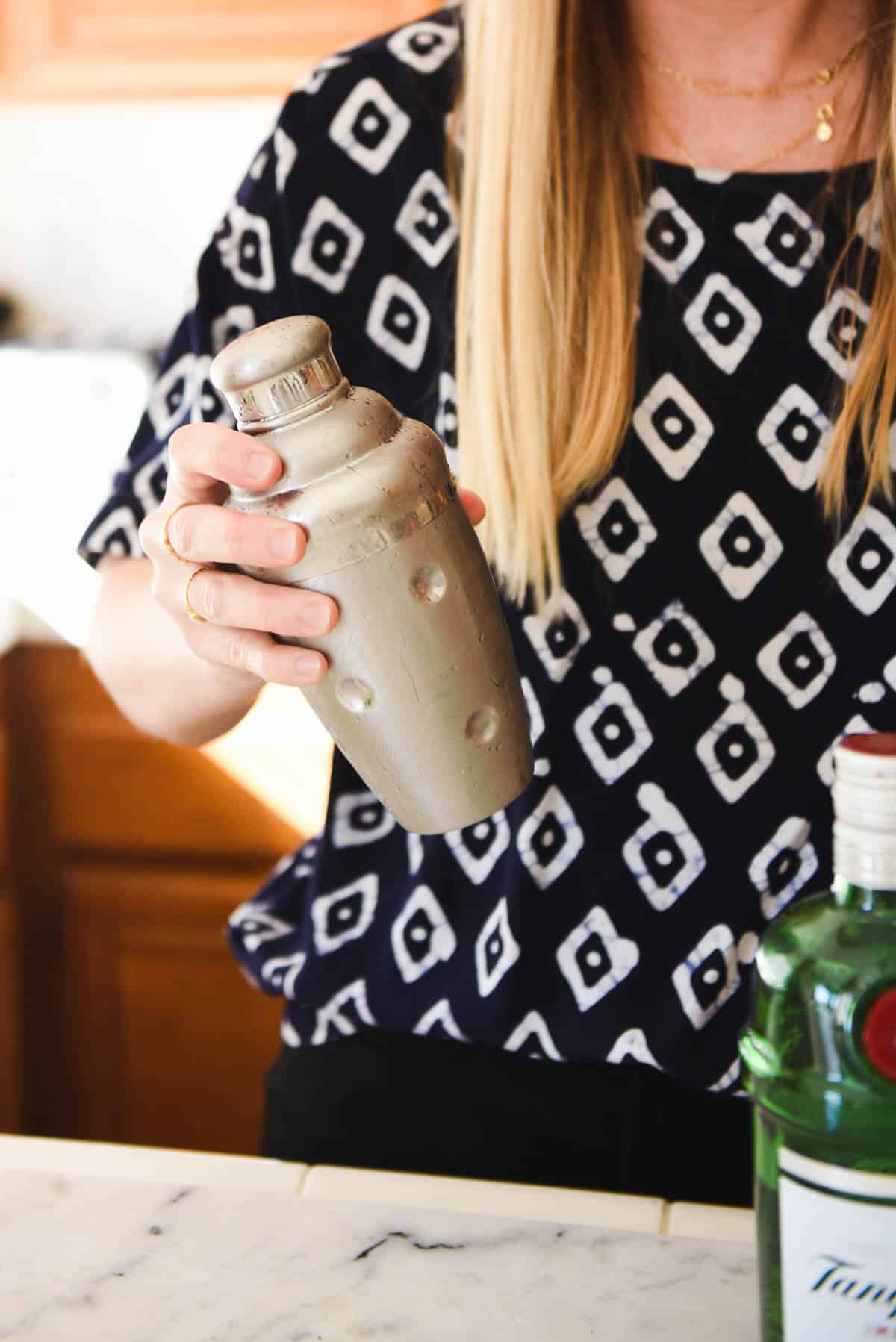 Woman in a black and white top shaking a silver cocktail shaker.