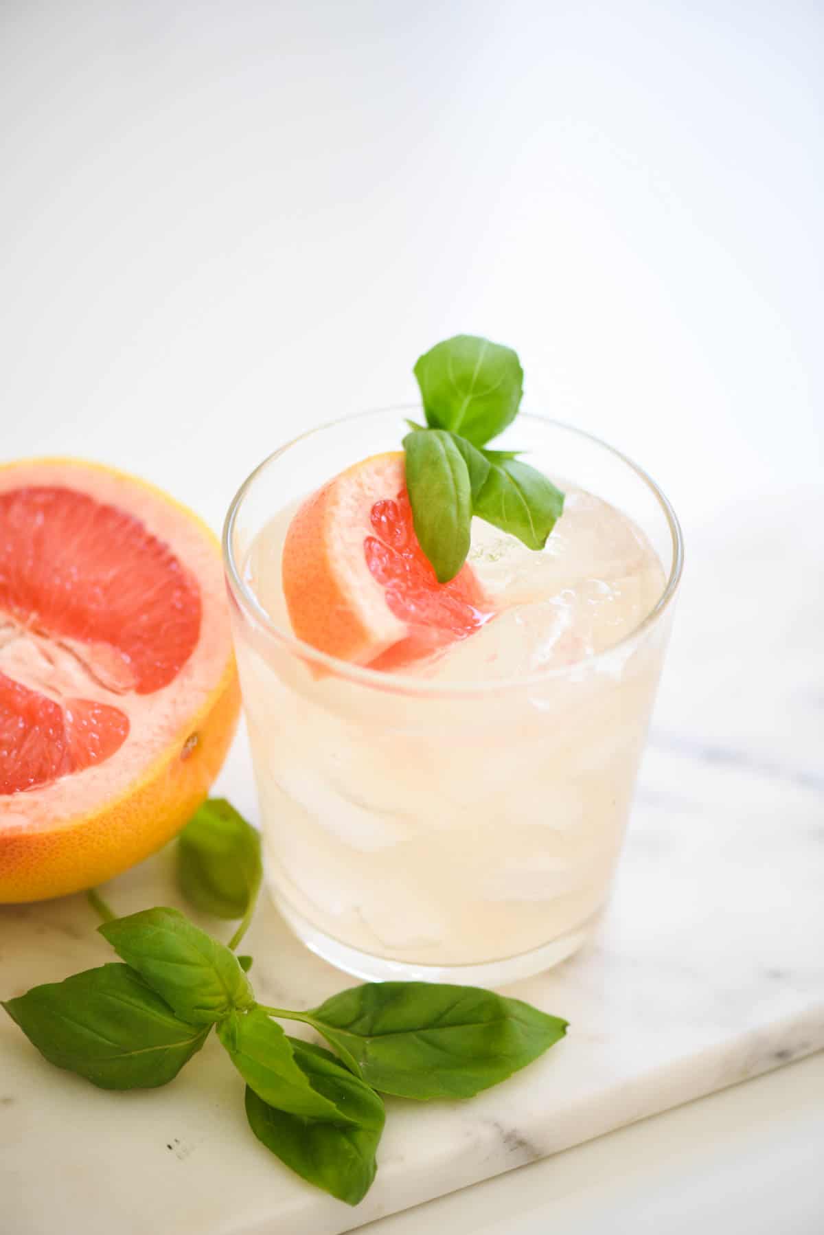A grapefruit cocktail on a white marble board garnished with fresh basil.