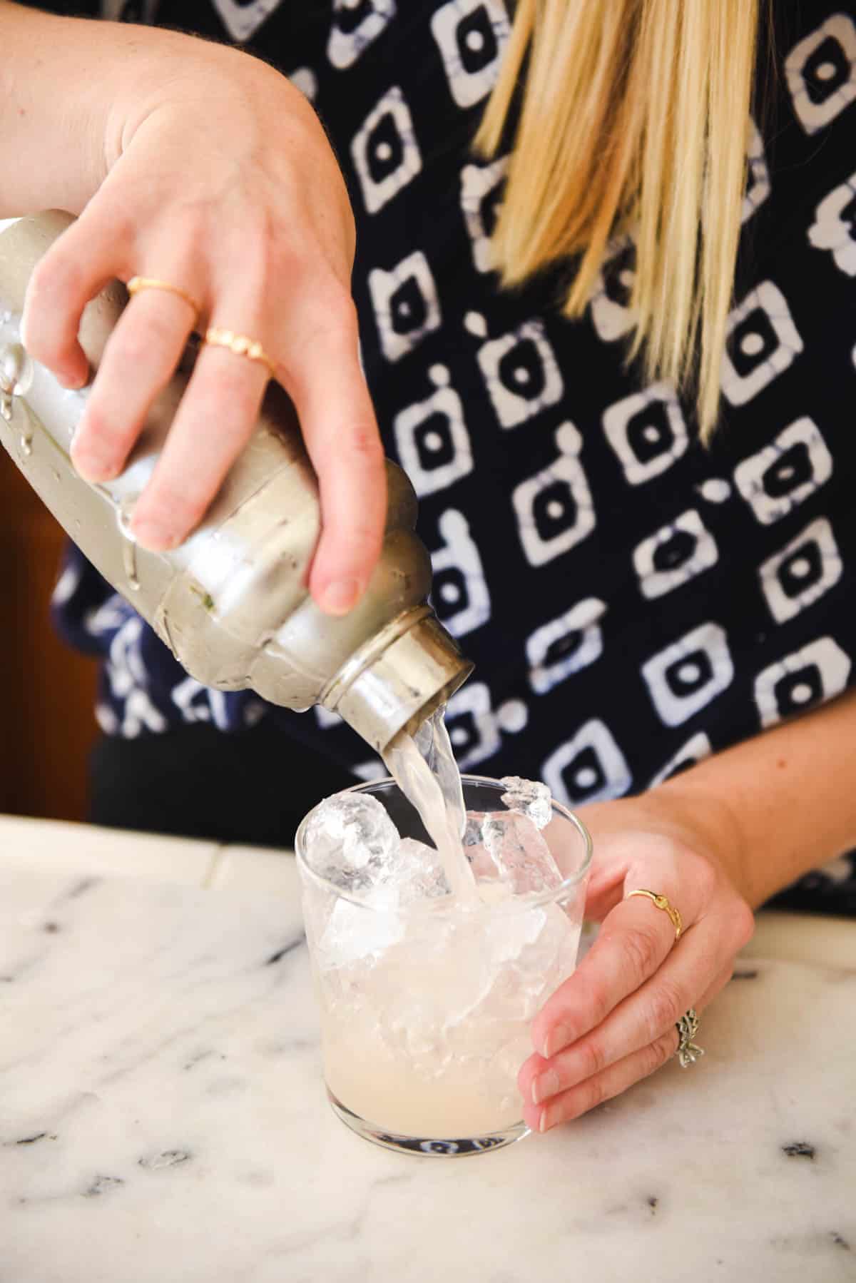 Woman pouring a grapefruit juice cocktail into a tumbler of ice.