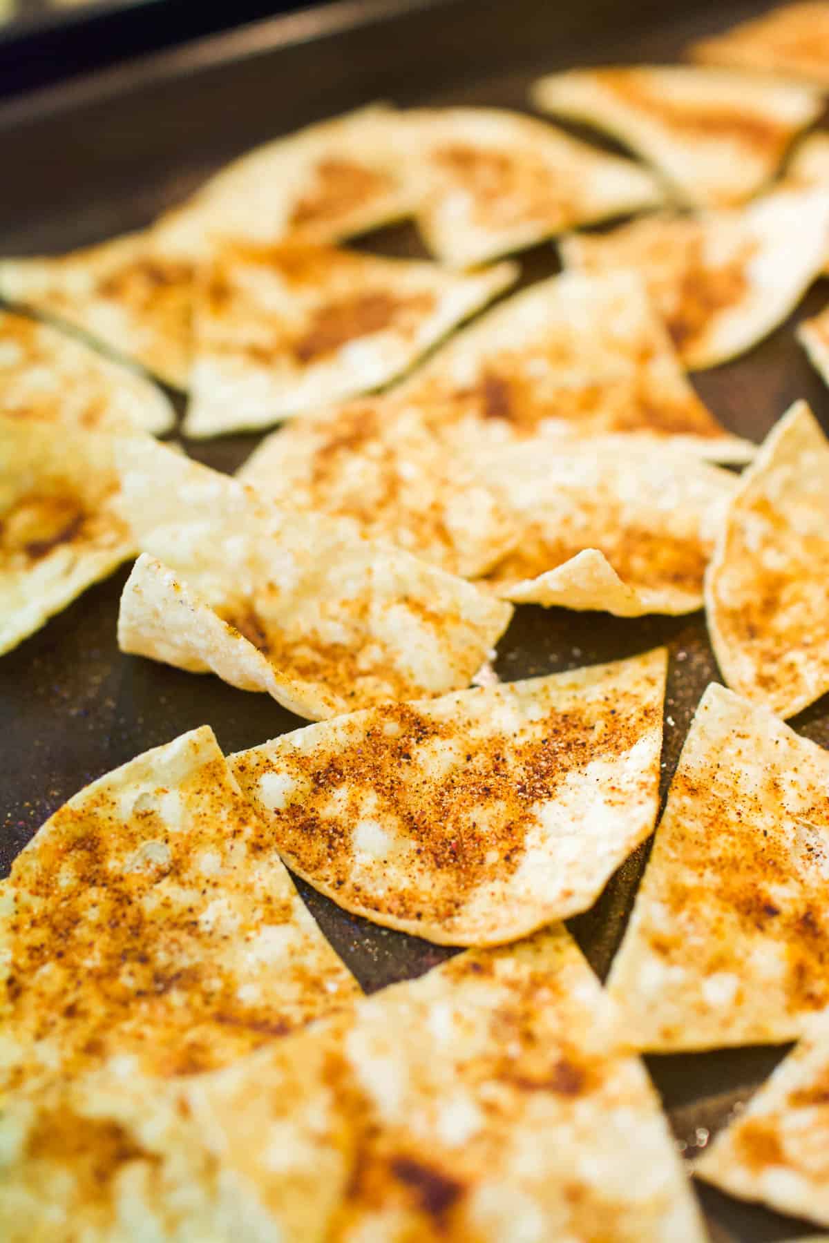 Close up image of seasoned and baked tortilla chips on a sheet pan.