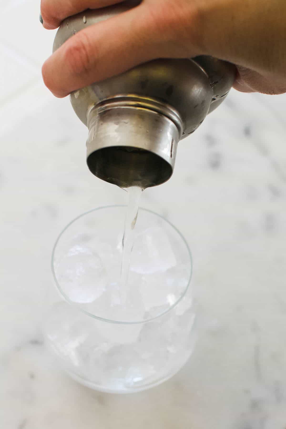 Cocktail being poured into a glass of ice from a cocktail shaker.