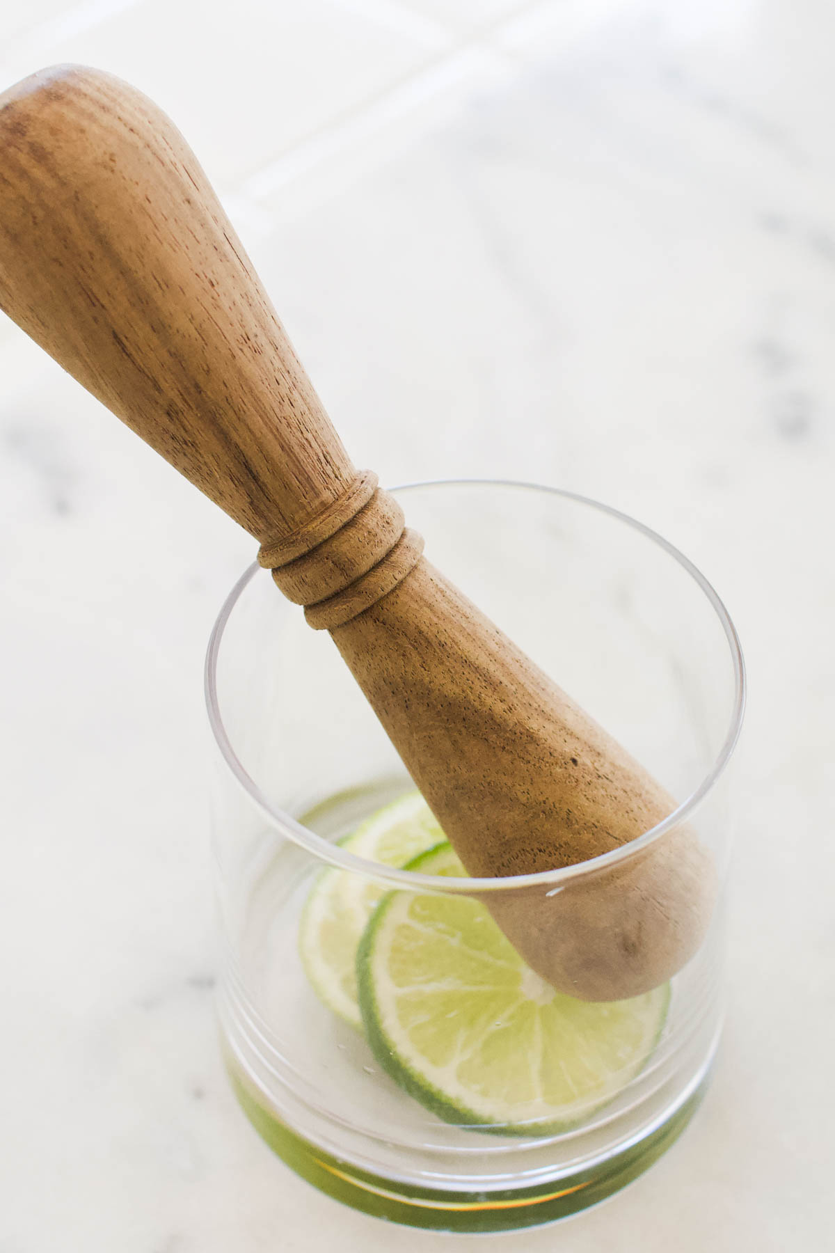 Slices of lime being muddled in a tumbler.