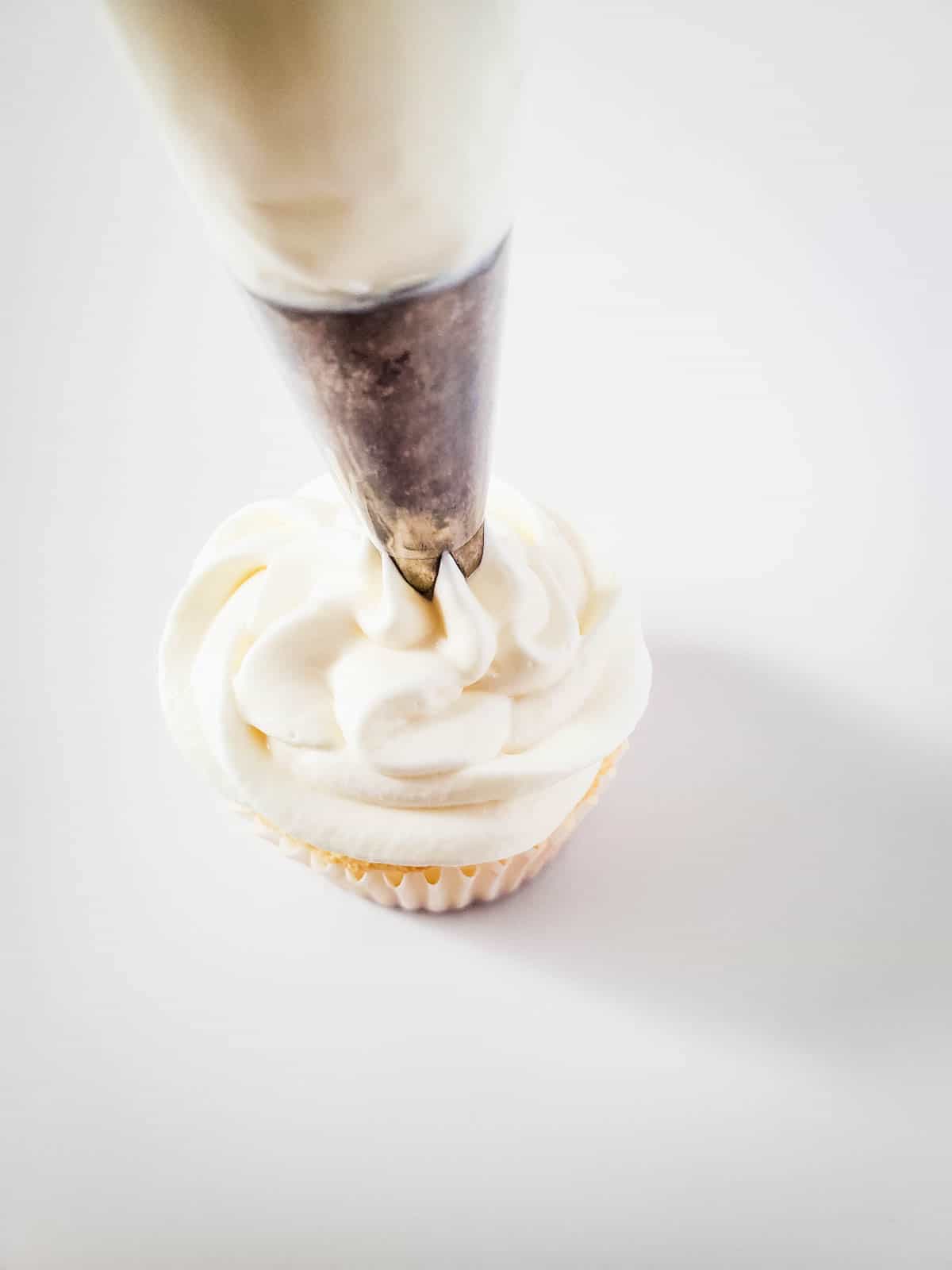 An angel food cake cupcake being frosting with white frosting.
