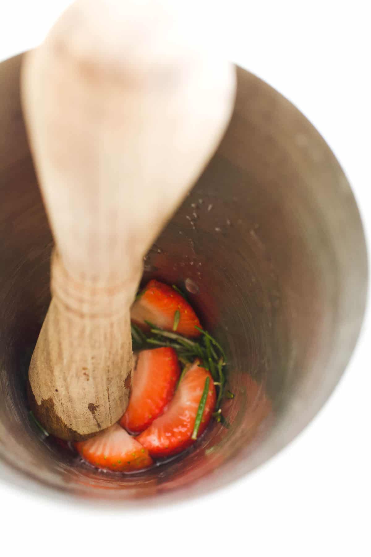 Muddling fresh strawberries and rosemary in a cocktail shaker.