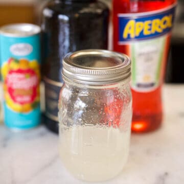 Jar of simple syrup on the counter with cocktail ingredients in the background.