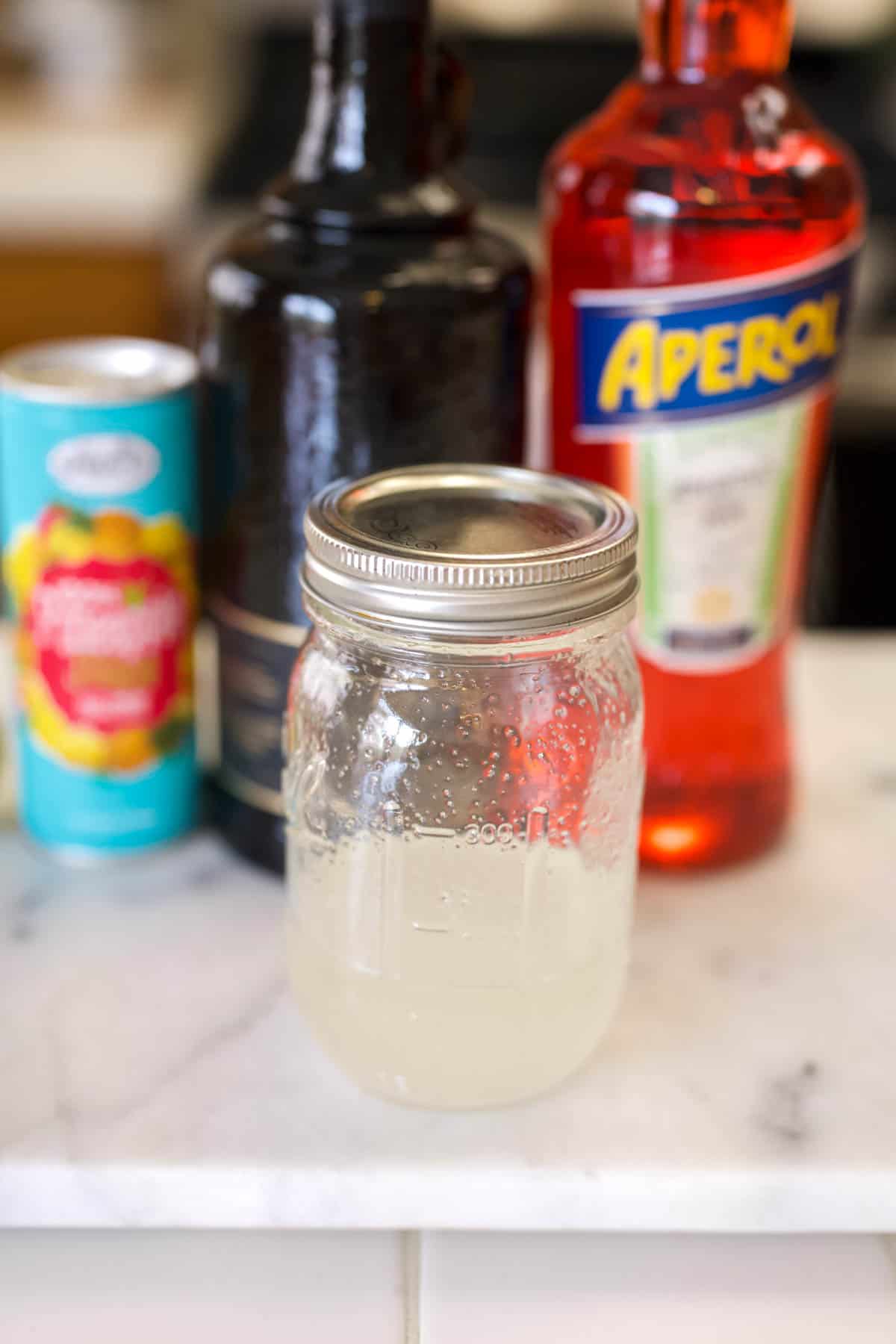 Jar of simple syrup on the counter with cocktail ingredients in the background.