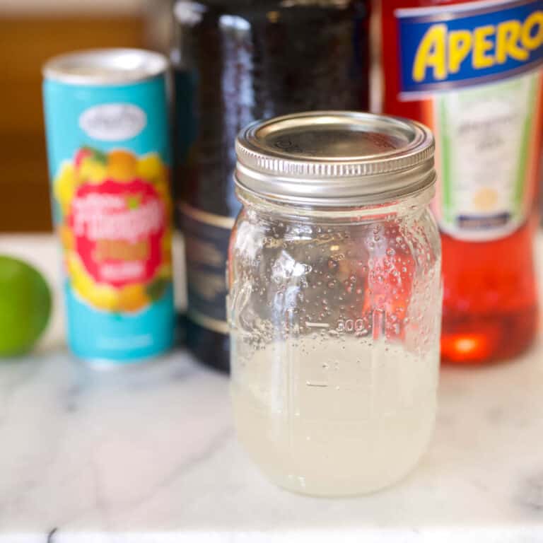 Jar of simple syrup on the counter with cocktail ingredients in the background.