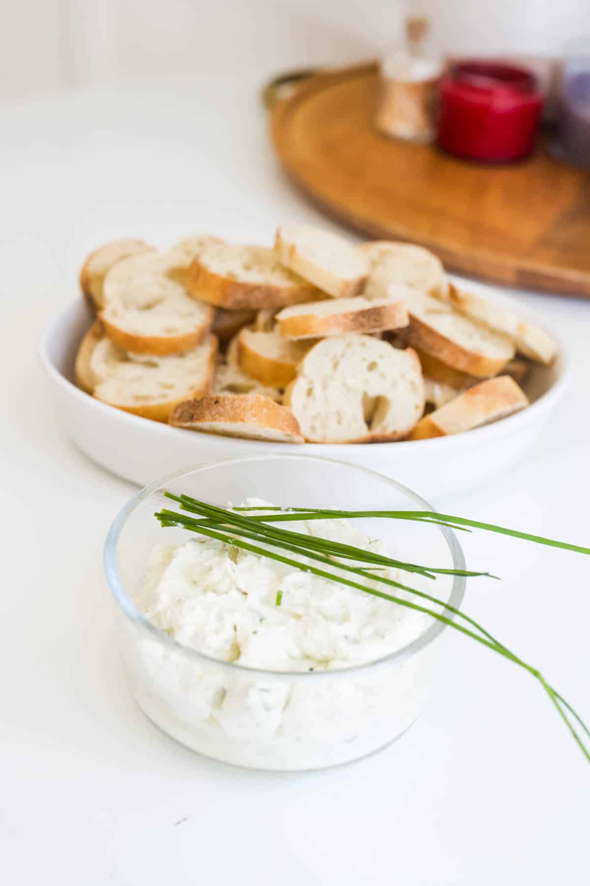 Cold burrata dip with chives in front of a bowl of bread to dip.