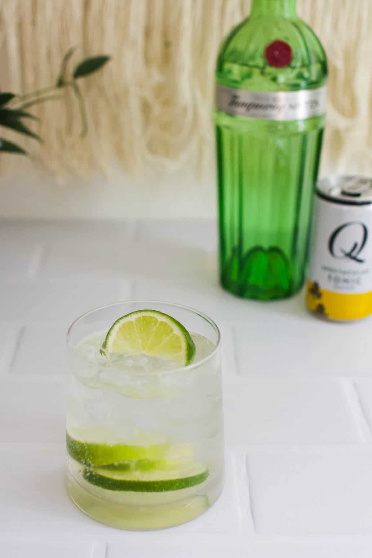 Gin and tonic on a white countertop with the bottle of gin and can of tonic water in the background.