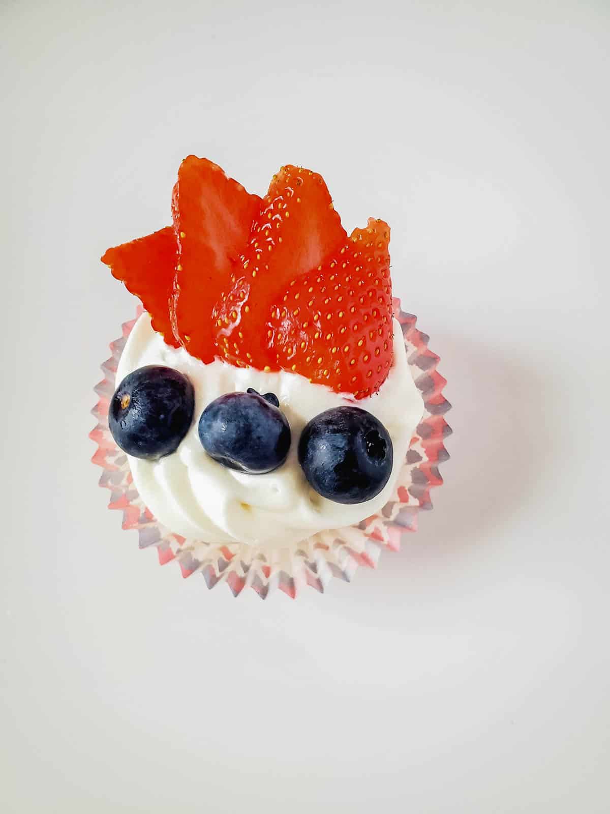 An angel food cake cupcake topped with white frosting and berries for 4th of July.