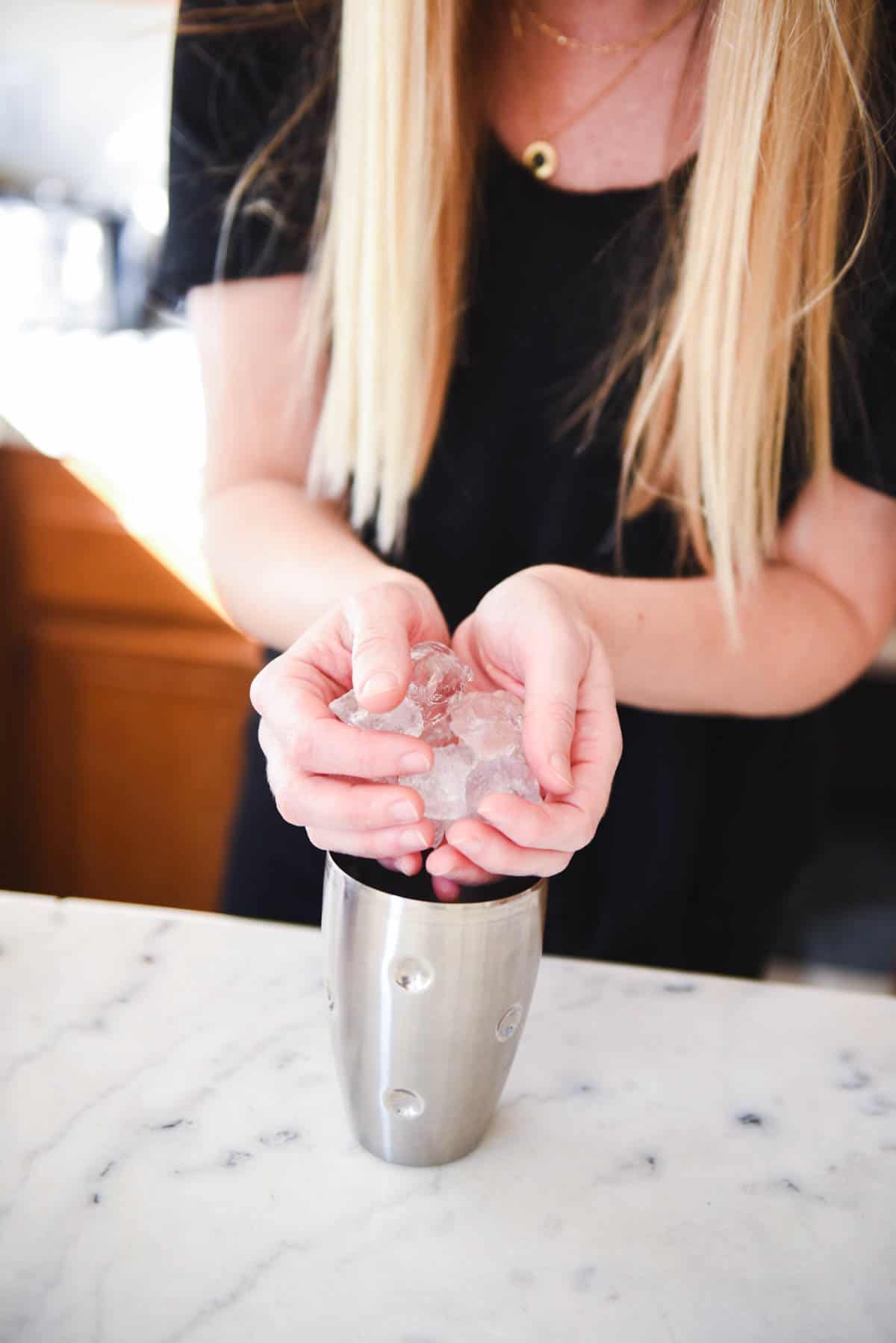 Woman adding ice to a cocktail shaker.