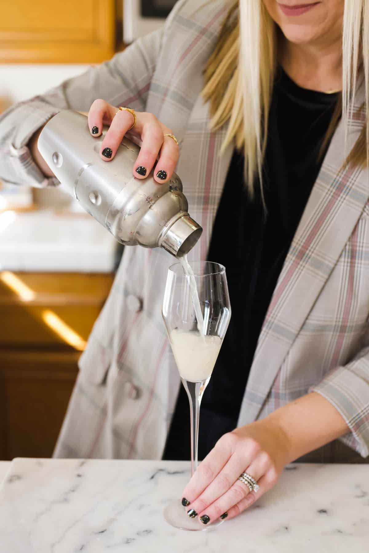 Woman pouring lemon juice from a cocktail shaker into a champagne flute.