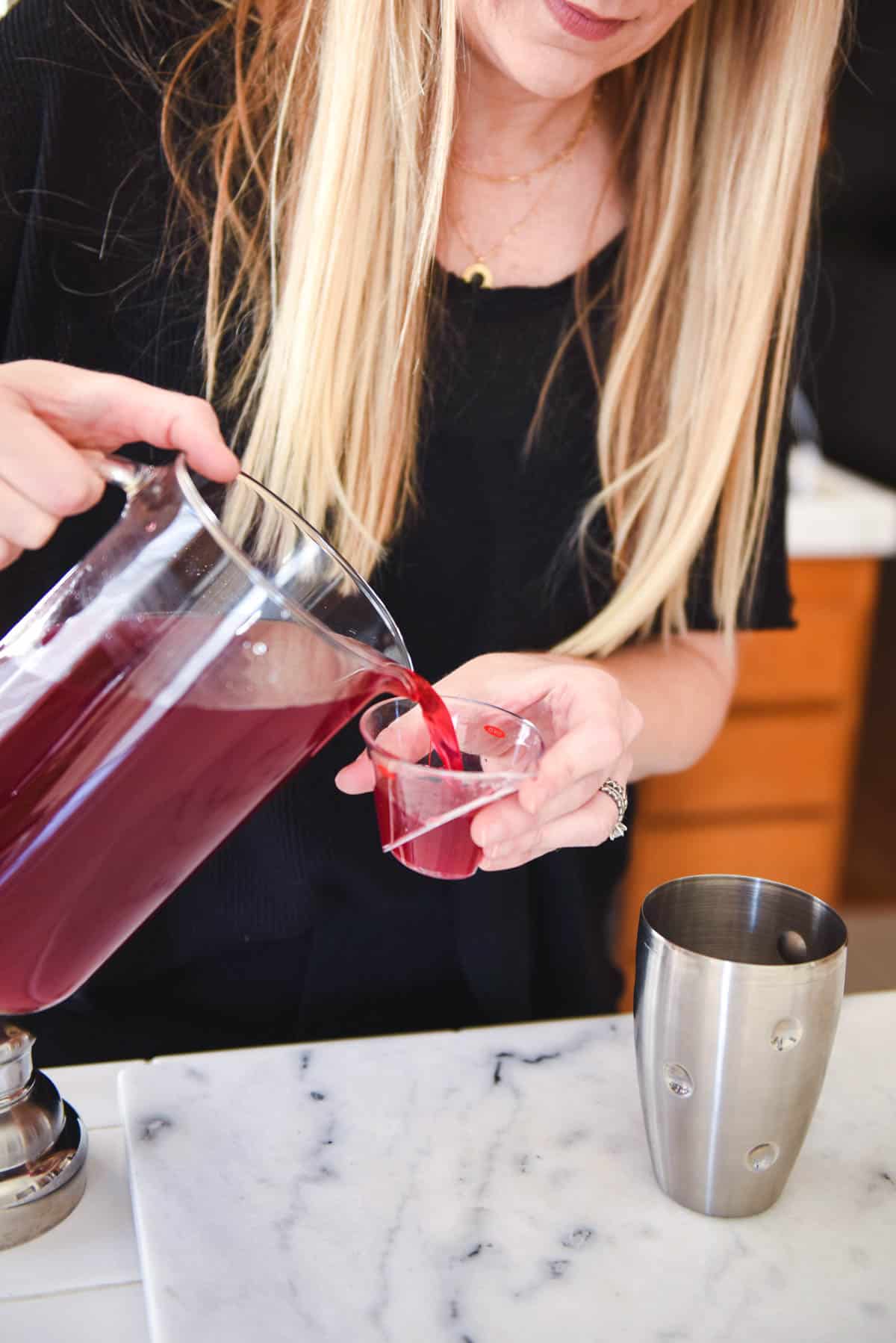 Woman adding blueberry lemonade to a measuring cup.