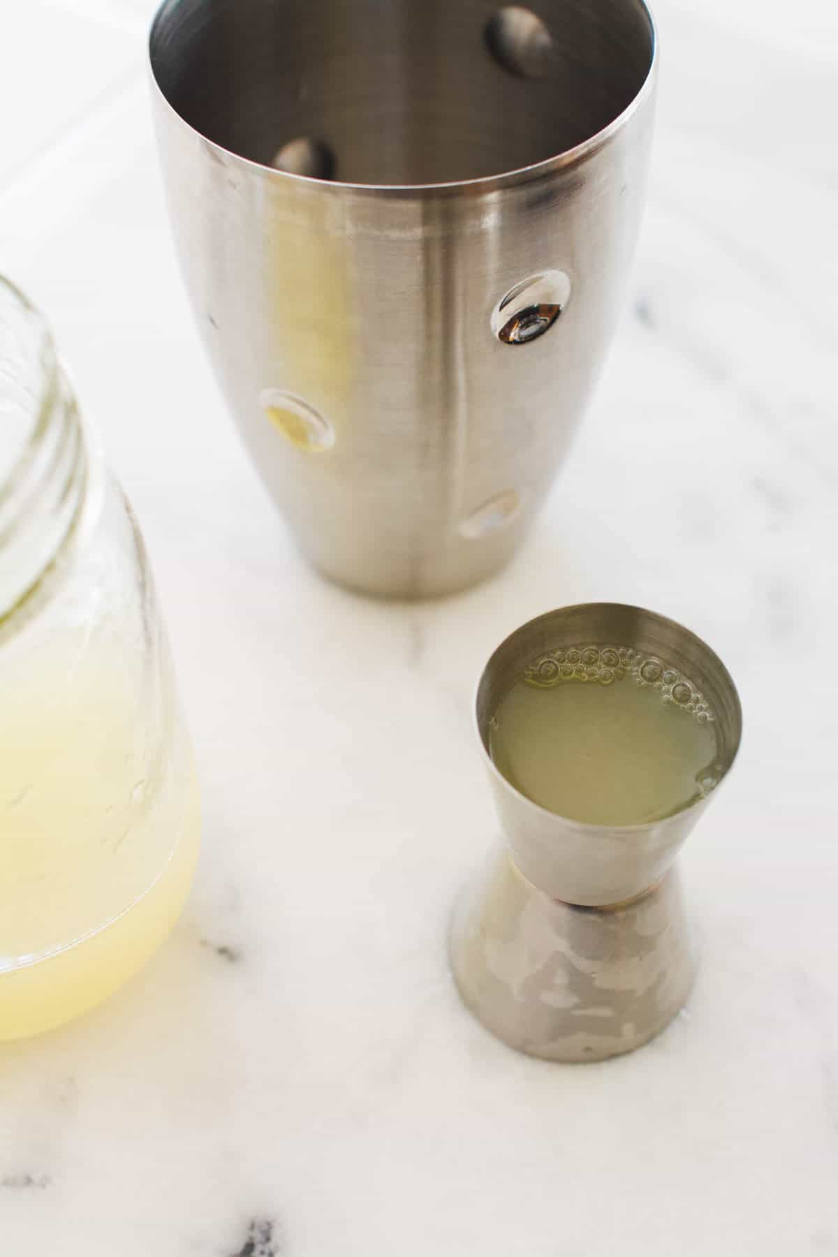 Jigger full of lemon juice next to a cocktail shaker.