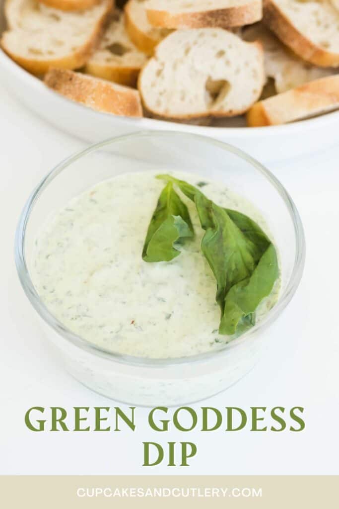 Text: Green Goddess Dip, under a glass bowl of dip topped with fresh basil in front of a bowl of bread.