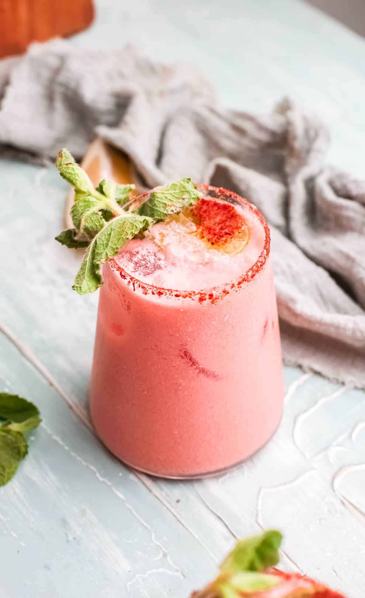 A pink cocktail in a short glass with a pink salt rim and mint garnish.