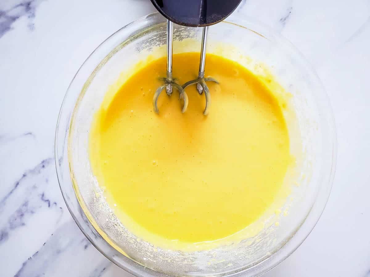 Mixing a yellow cake batter in a large glass bowl with a handmixer.