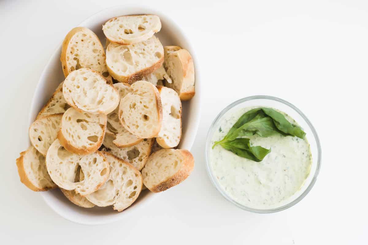 A bowl of green goddess dip topped with basil next to a bowl of bread.