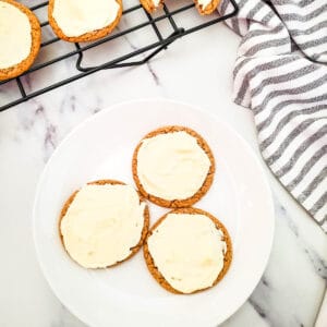 A white plate with frosted carrot cake cake mix cookies next to a towel and wire cooling rack.