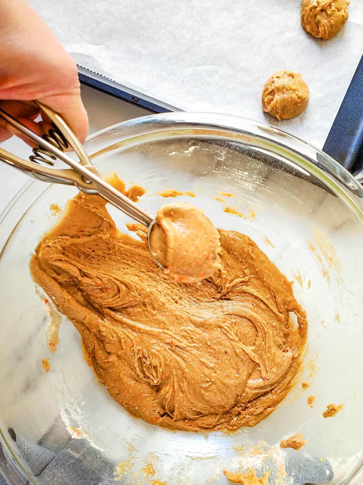 A bowl with cookie batter being scooped with a scopper.