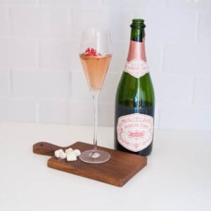 Champagne cocktail on a wooden board next to sugar cubes and a half full bottle of pink champagne.