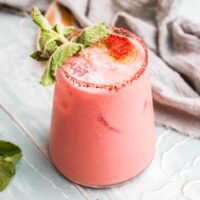 A stemless wine glass with a pink cocktail made from coconut rum and Aperol on a table.