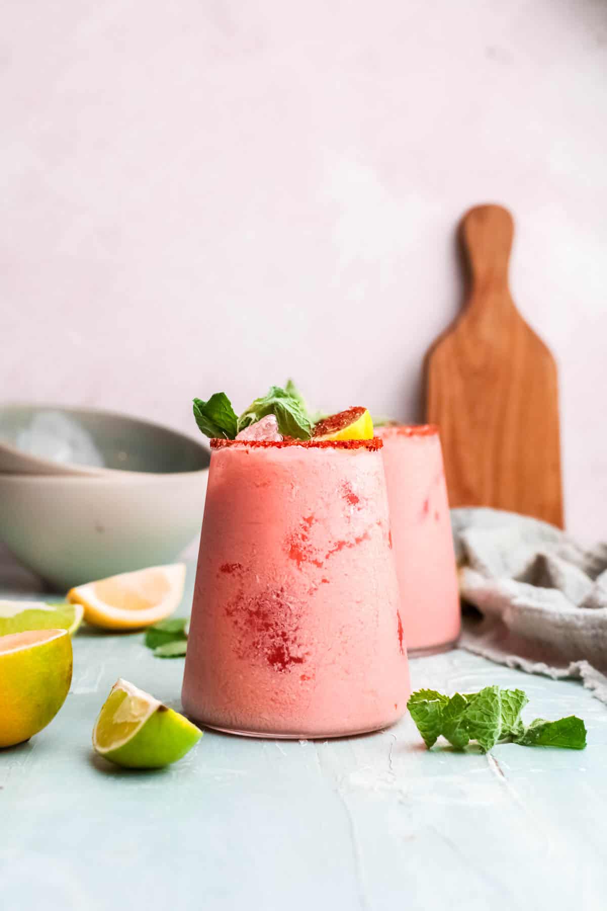 A creamy coconut daiquiri with Aperol in a short cocktail glass on a table with ingredients around it.