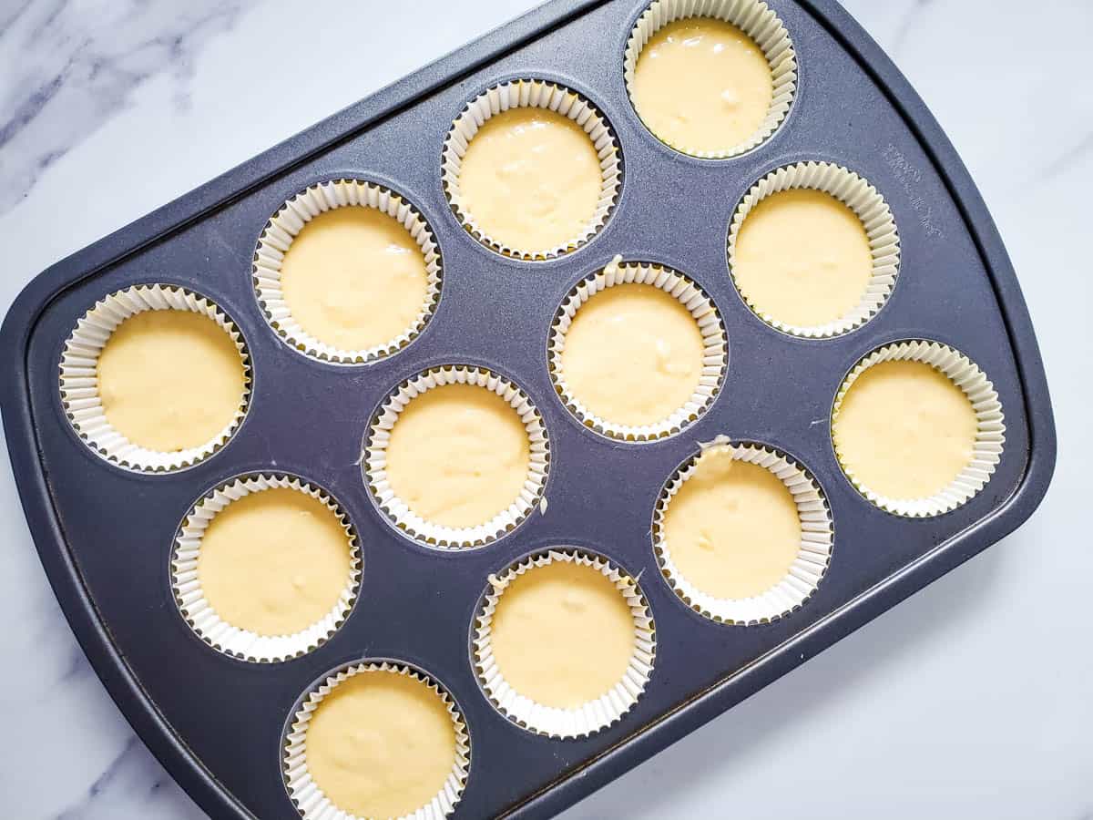 A muffin tin lined with cupcake liners holding cupcake batter.
