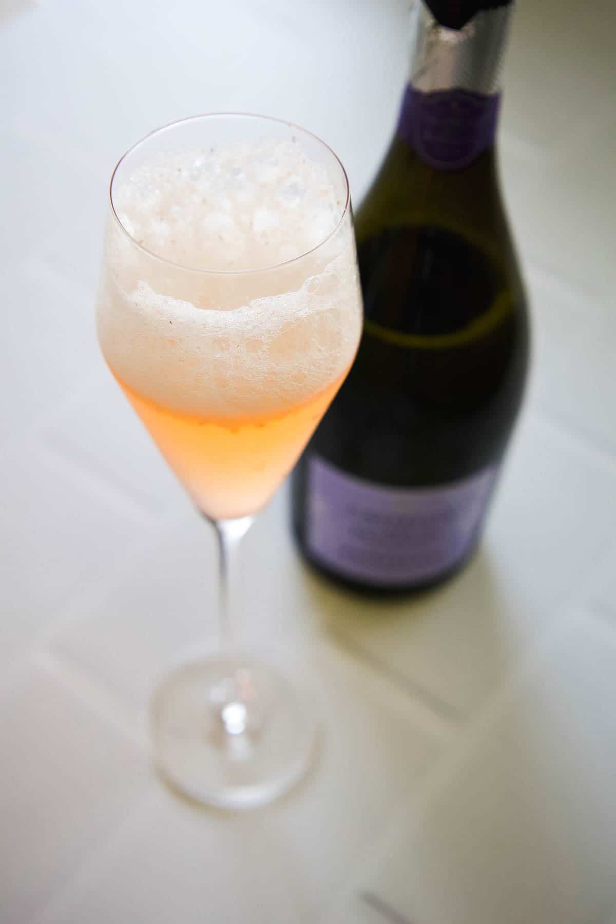 A champagne flute with a st germain cocktail next to a bottle of prosecco.