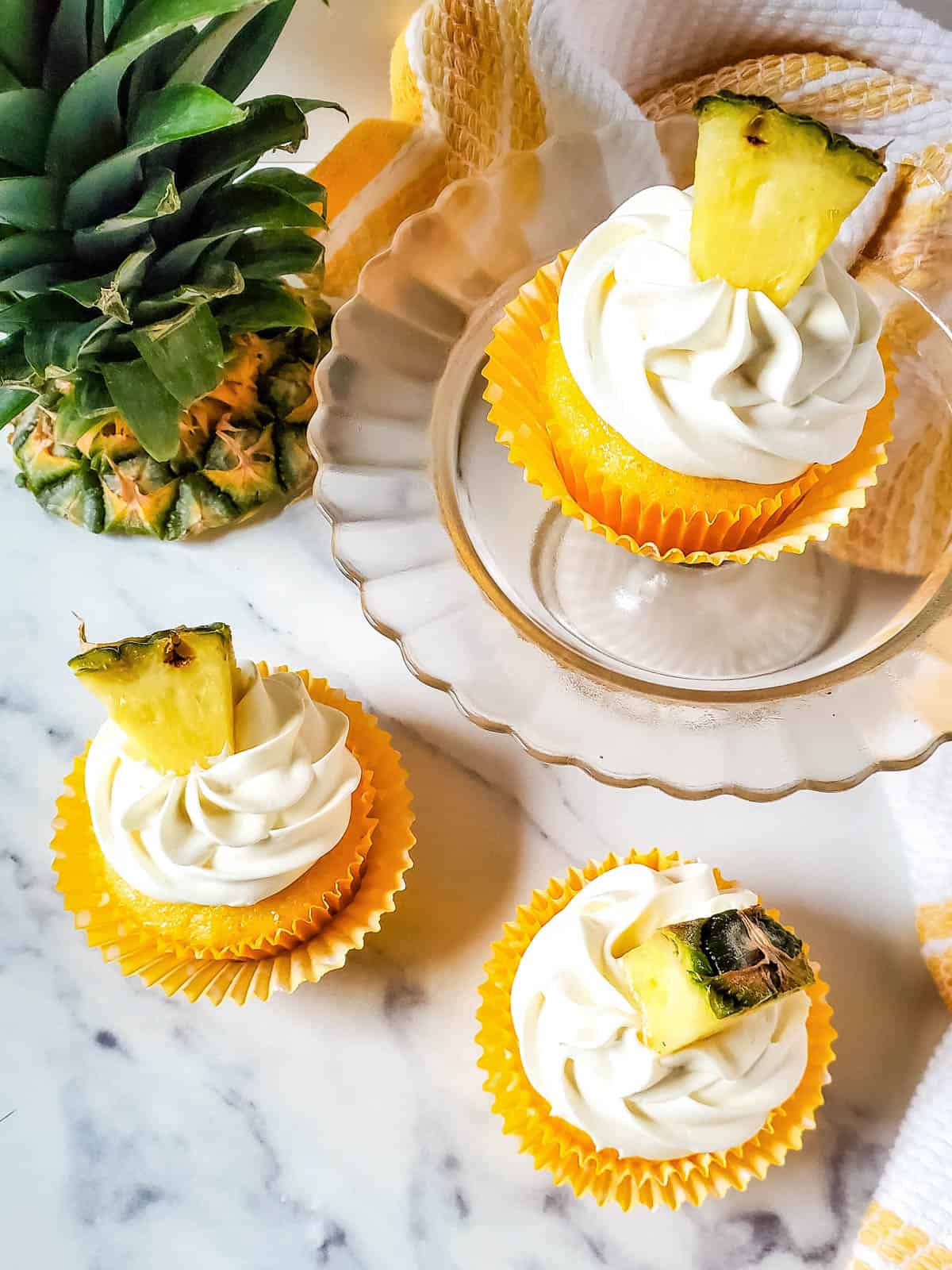 Three pineapple cupcakes on a white counter top.