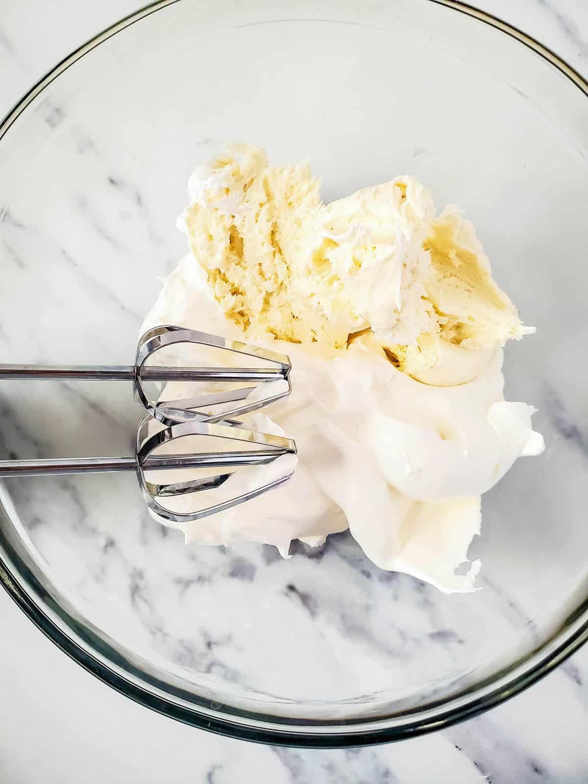 A large glass mixing bowl filled with the ingredients for frosting for pineapple cupcakes.