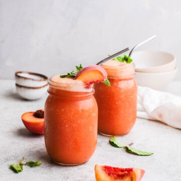 Two servings of rose wine blitzed with fresh peaches in jars with metal straws on a grey background.