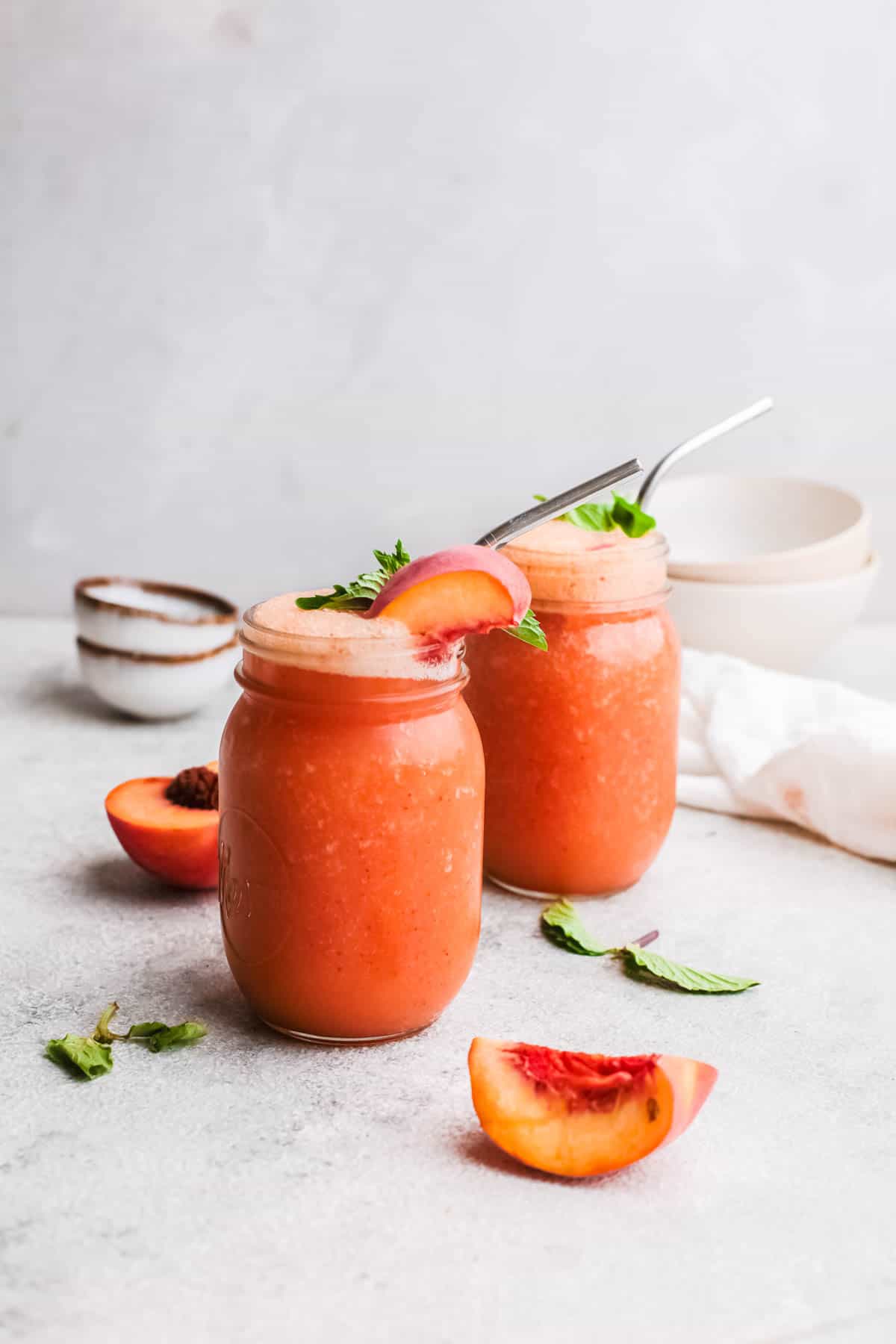 Two servings of rose wine blitzed with fresh peaches in jars with metal straws on a grey background.