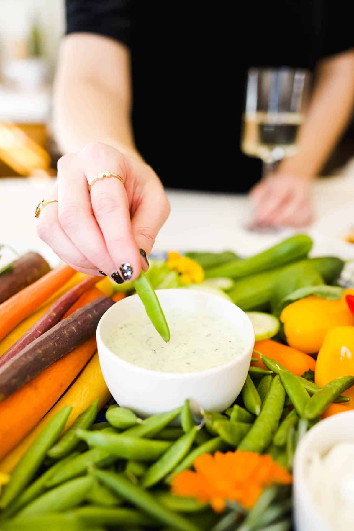 A woman dipping fresh vegetables in green dip.