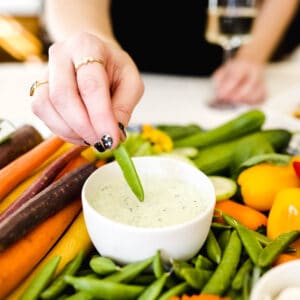 A woman dipping a snap pea in green goddess dip.