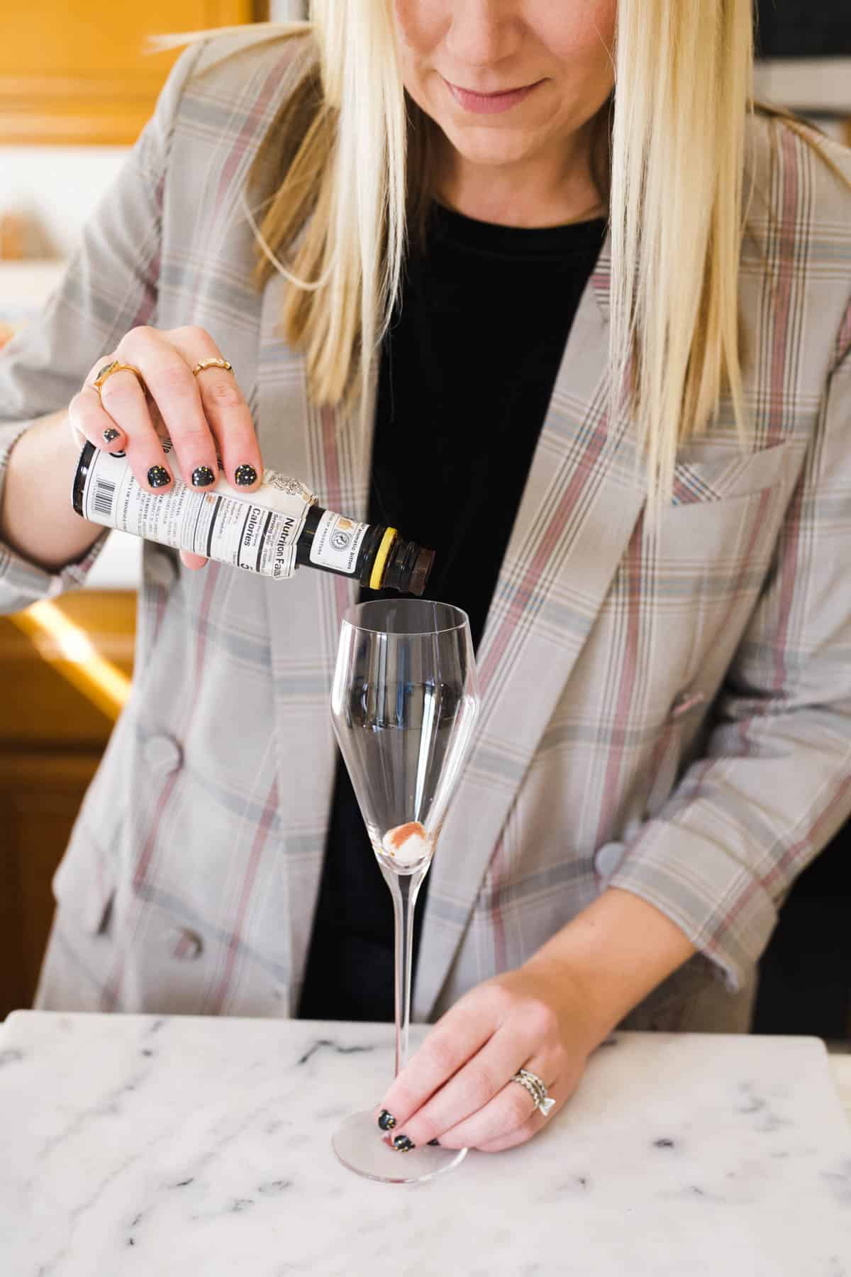 Woman pouring cocktail bitters over a sugar cube in a champagne flute.