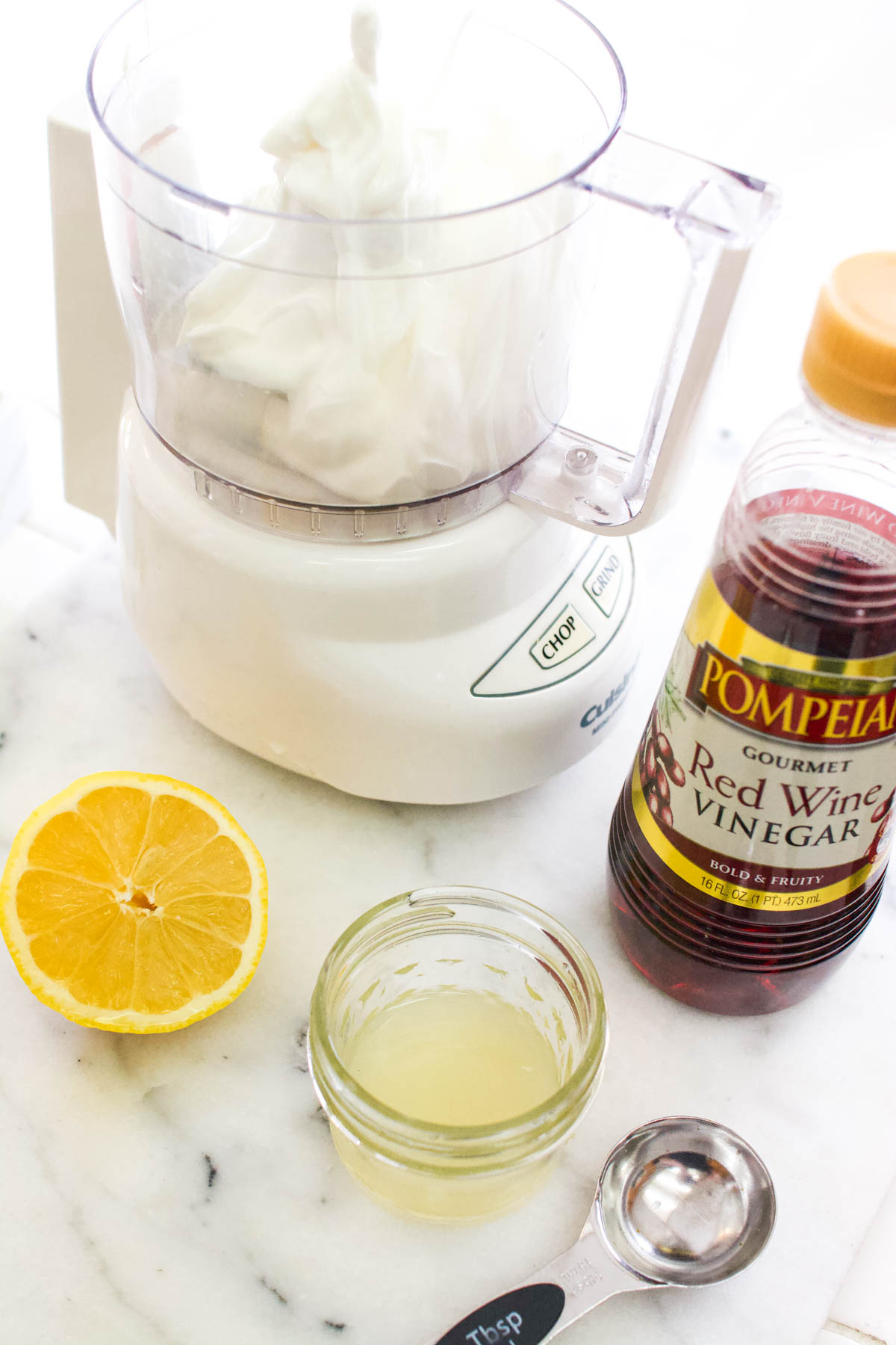 A food processor next to red wine vinegar, lemon juice, and a sliced lemon.