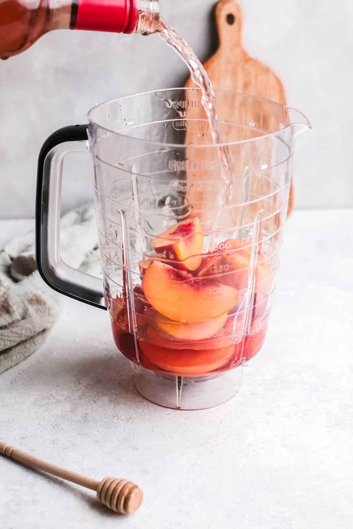 Wine being poured into a blender with quartered fresh peaches.