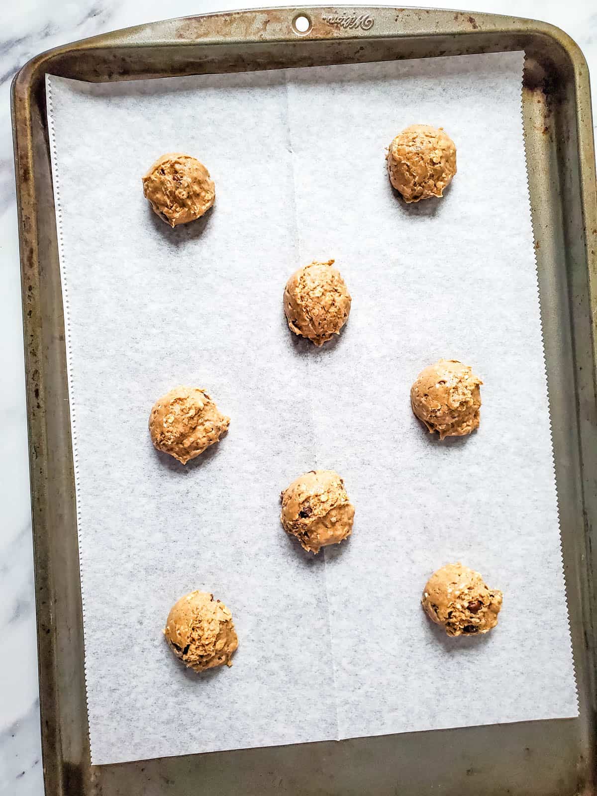 Chocolate chip oatmeal cake mix cookie dough scooped into balls on a parchment lined cookie sheet.