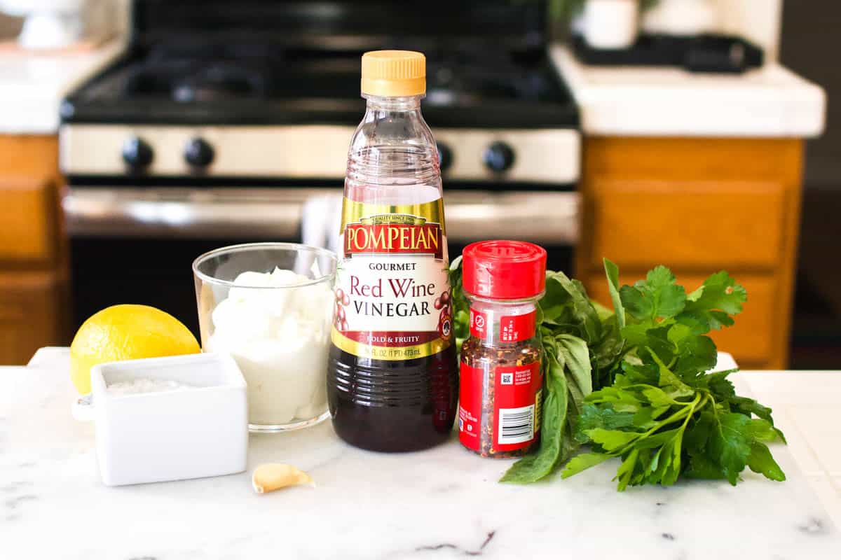 The ingredients to make green goddess dip on a white marble counter top.